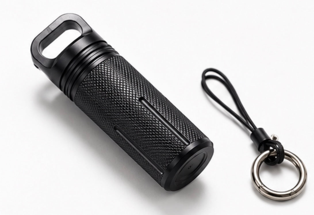 A black textured cylindrical keychain with a looped handle and a black lanyard attached to a silver metal key ring, photographed on a clean white background.