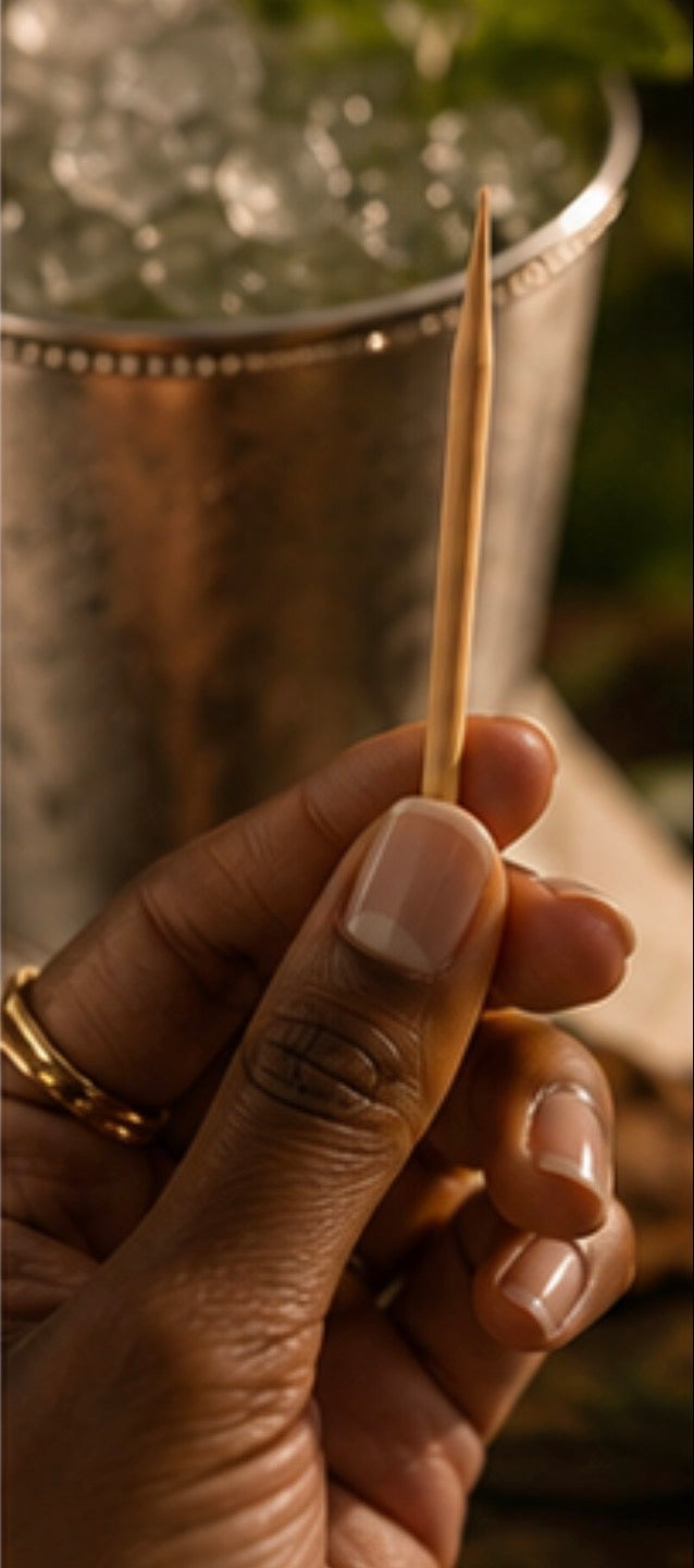 Hand holding a Cinder Pick with a silver cup of ice in the background