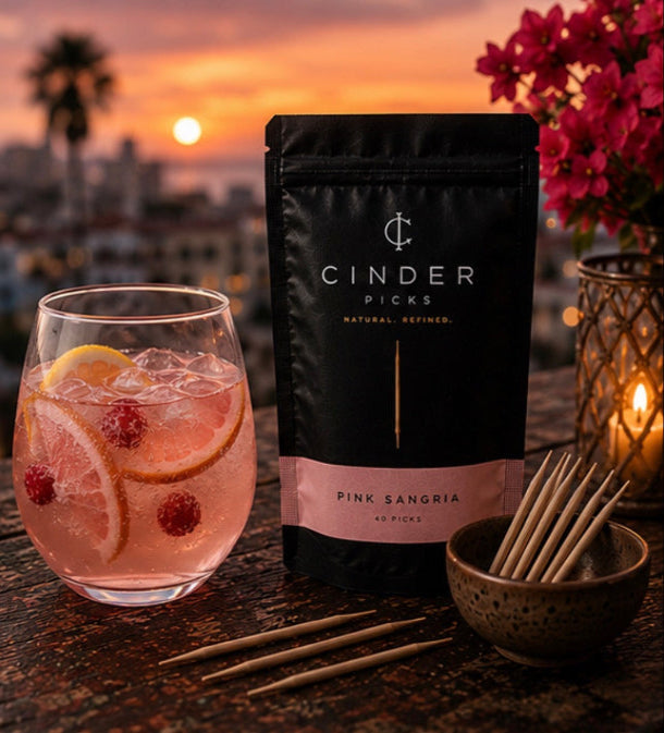 Cinder Picks Pink Sangria package with a glass of pink sangria and lemon slices on a sunset background.