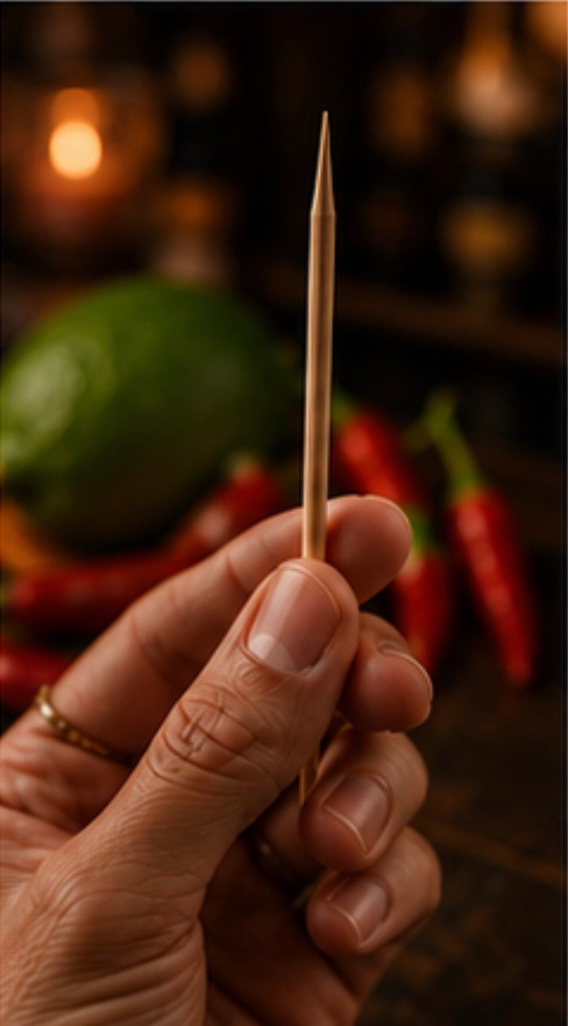 Hand holding a Cinder Pick with a blurred background of chilli and lime.