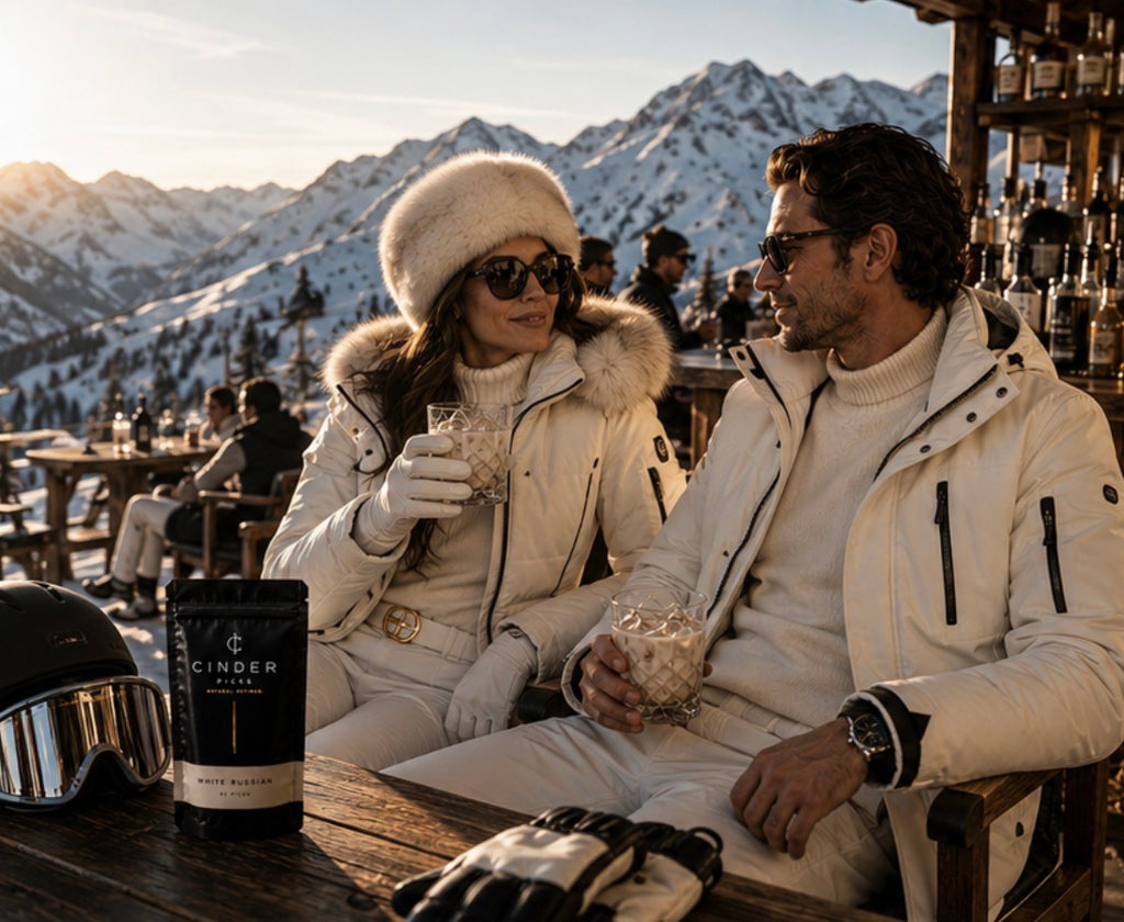 Two people in winter clothing sitting at a mountain lodge with snow-covered peaks in the background.