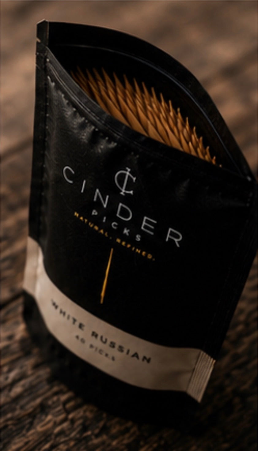 Packaged guitar picks with 'Cinder Picks' branding on a wooden surface