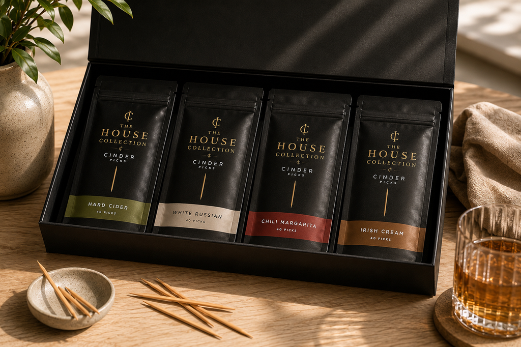 Four pouches of 'The House Collection' flavoured picks in a black box on a wooden table garnishes.