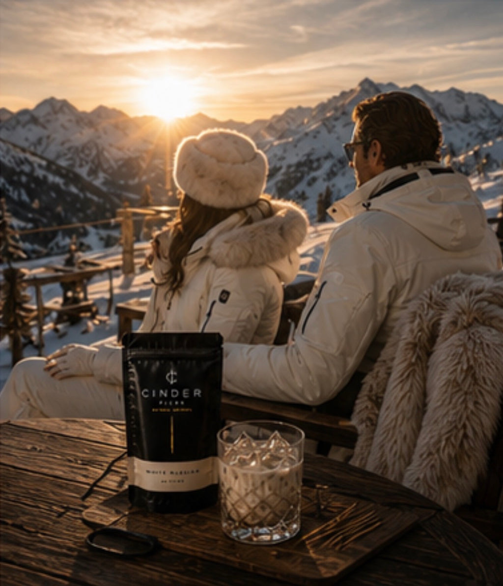 Two people enjoying a sunset view with a pouch of Cinder Picks placed on a table on a snowy mountain.